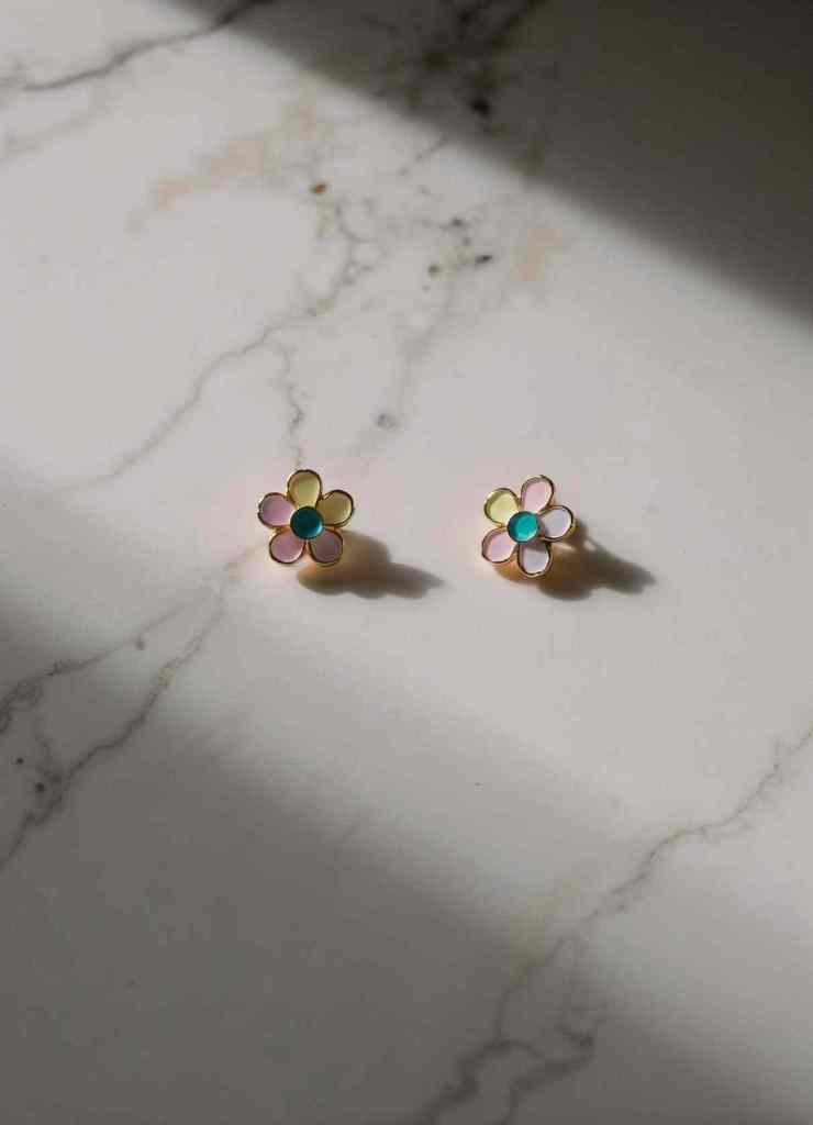 A pair of pastel-hued flower earrings resting on a marble surface. The earrings feature multicolored petals with a blue center, offering a soft, elegant charm perfect for everyday wear.